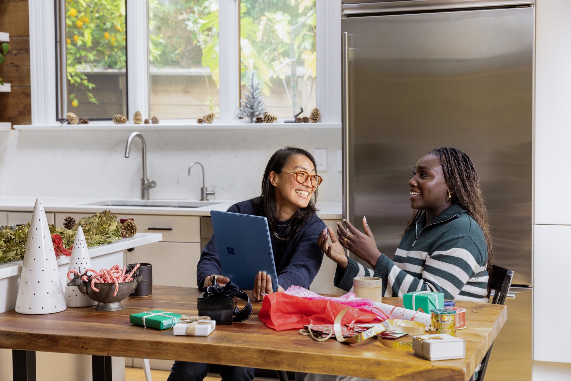 Two women sitting together in the kitchen, using a laptop at a table.